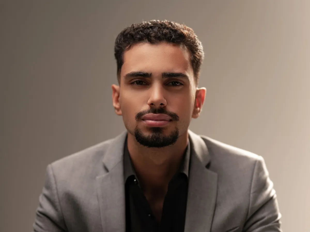 Fabrício Júnior, de blazer cinza e camisa preta, em retrato de estúdio