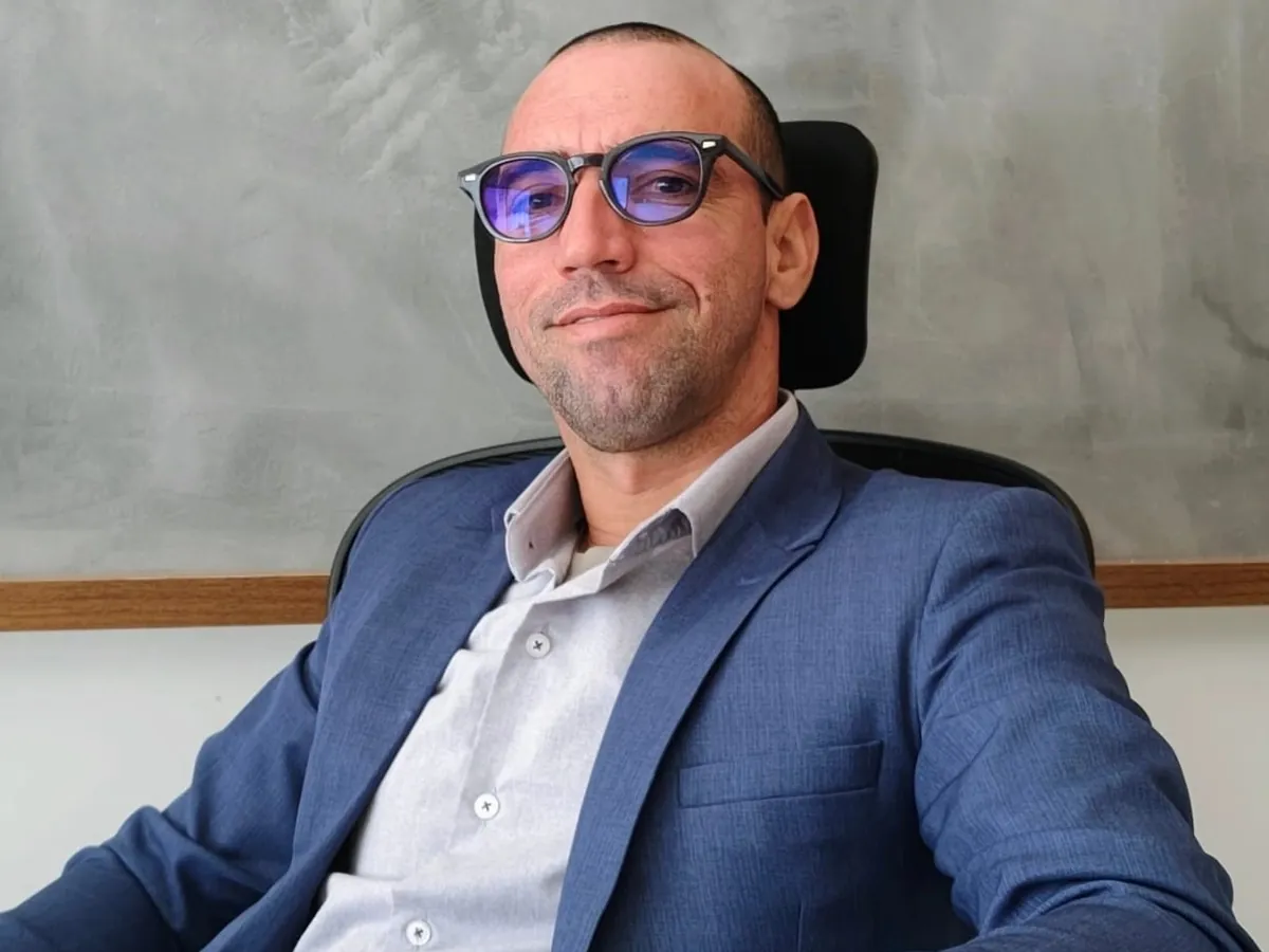 Paulo Ramos, de terno azul e óculos, sentado à mesa do escritório